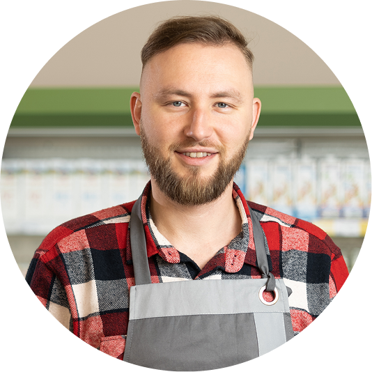 A man smiling wearing an apron standing in milk aisle of a grocery store holding a tablet