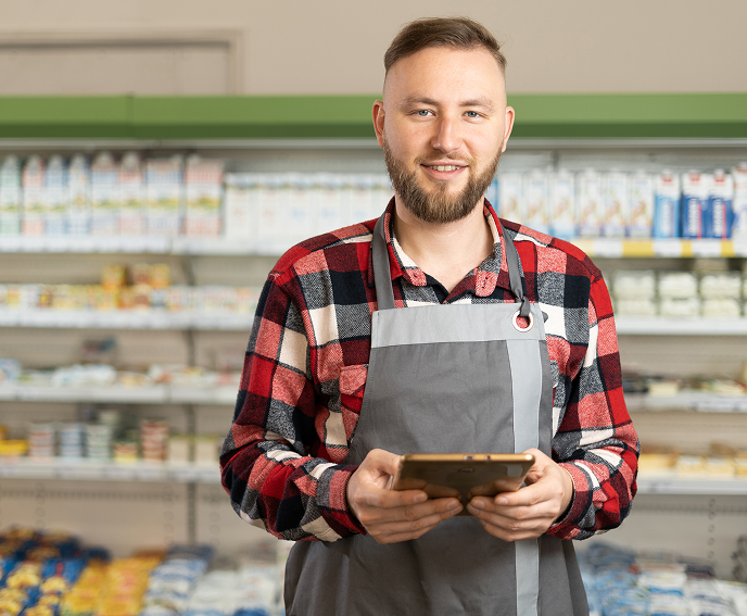 A man smiling wearing an apron standing in milk aisle of a grocery store holding a tablet