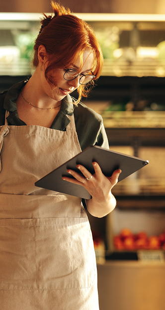 Woman wearing apron looking at tablet in a grocery store