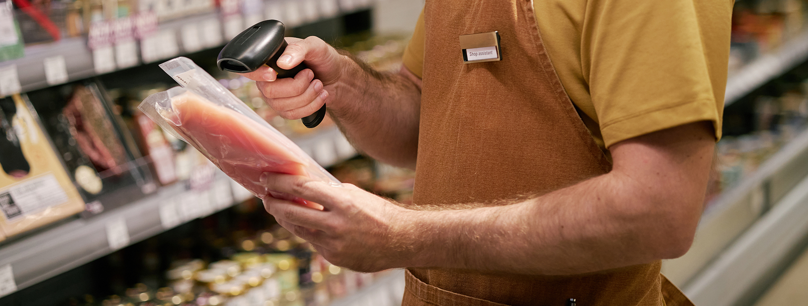 A man wearing an apron is scanning a meat package item in a grocery store